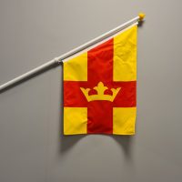 Svenska kyrkans flagga på en vit fasadflaggstång mot grå bakgrund